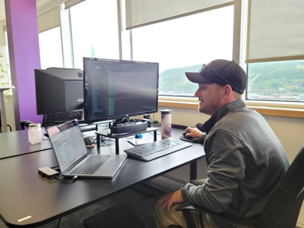 Adam coding at his desk, with the harbour and hills outside the window