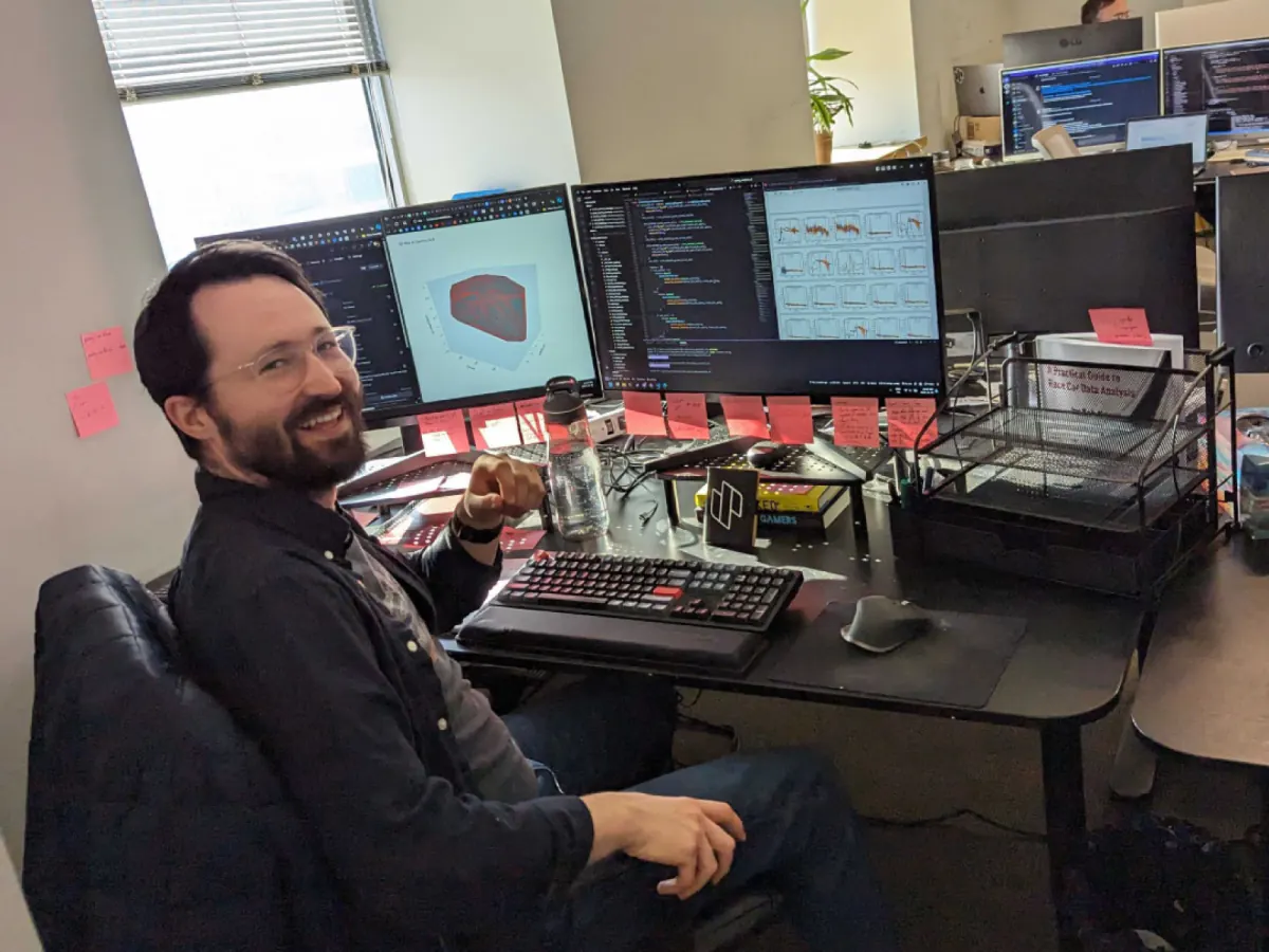 Scott Skanes at his desk with code and 3D models on his monitors